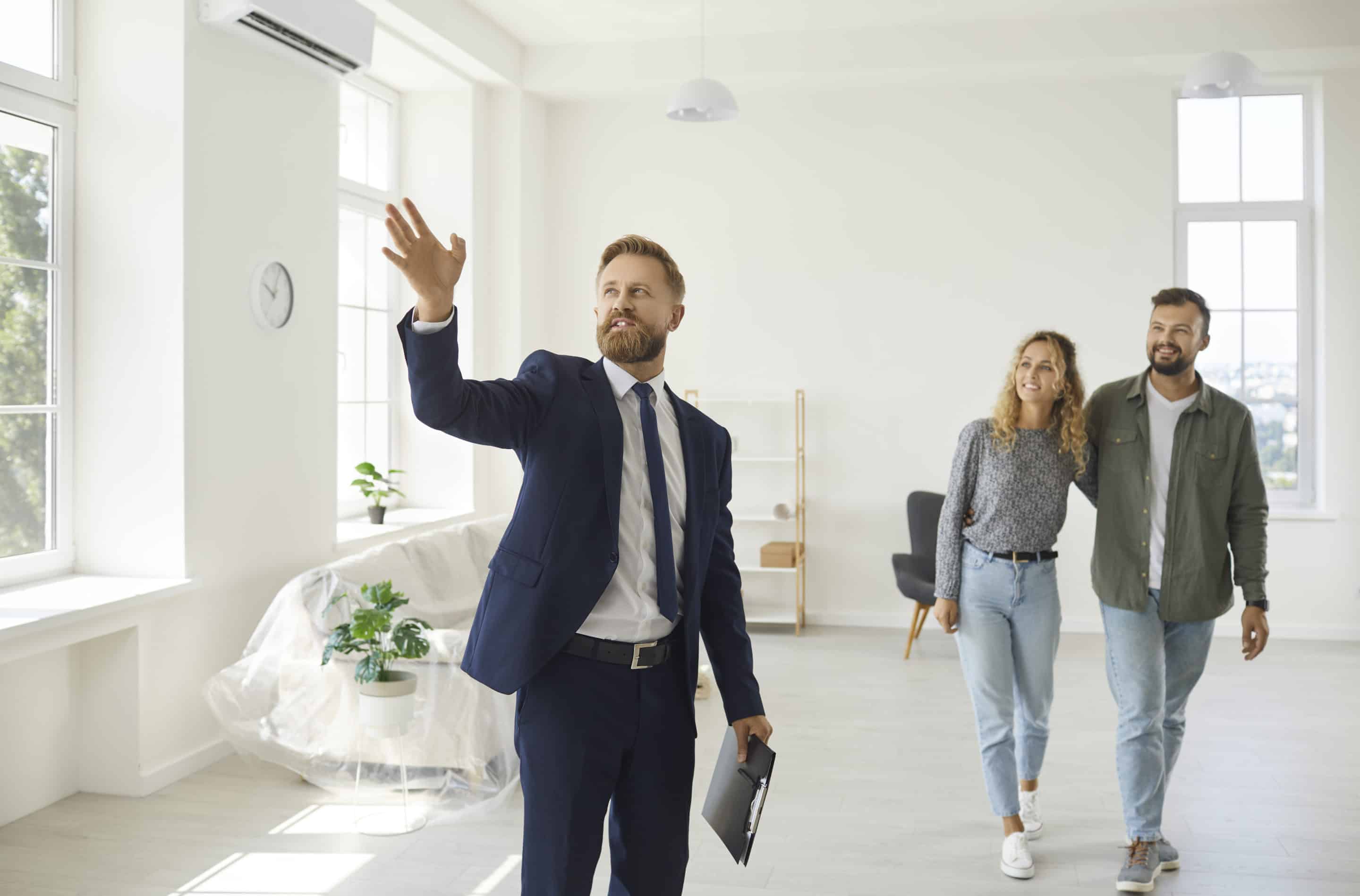 Real estate agent giving happy young customers a tour about a new spacious house